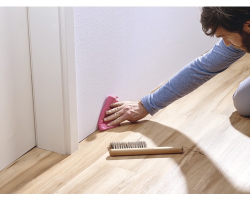 Mann reinigt Sockelleisten mit Tuch und Bürste