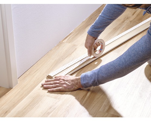 Person befestigt Klebeband an einer Sockelleiste.