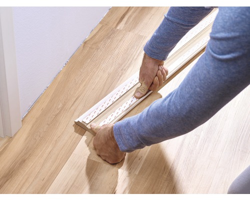Person befestigt Sockelleiste mit Klebestreifen am Boden.