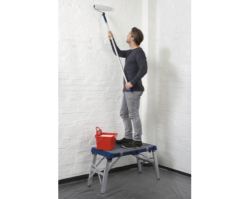 Un homme peint un mur avec un rouleau à peinture depuis un échafaudage.