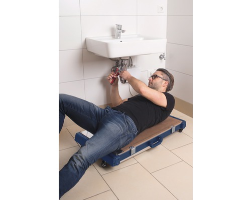 Installateur sur une planche à roulettes de montage réparant un lavabo