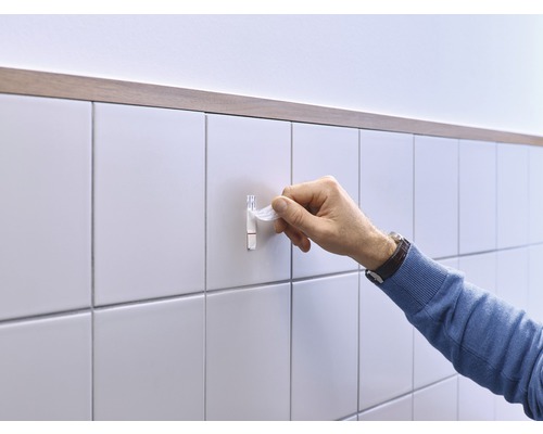 Eine Person befestigt einen Klebehaken an einer gefliesten Wand.