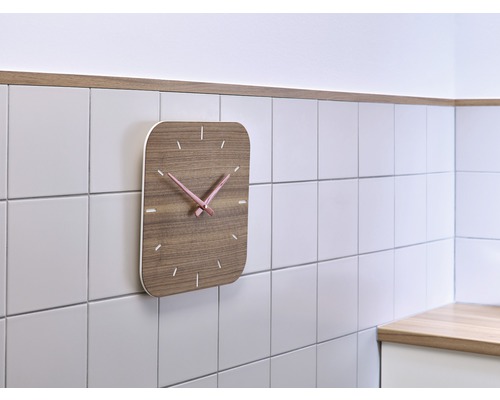 Wanduhr mit Holzoptik und rosafarbenen Zeigern an einer gefliesten Wand
