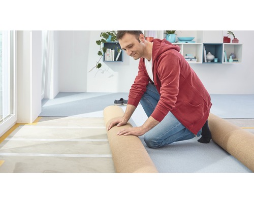 Un homme pose de la moquette dans une pièce lumineuse.