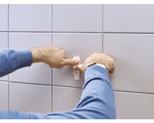 Une personne fixe un niveleur de carreaux sur un mur carrelé.