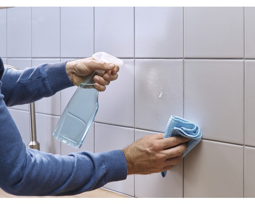 Une personne nettoie des carreaux avec un spray nettoyant et un chiffon.