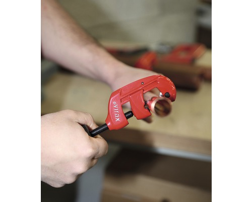 Une personne coupe un tube de cuivre avec un coupe-tube de la marque Virax.