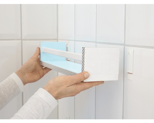 Une personne installe une étagère murale dans la salle de bain.