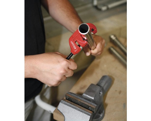 Une personne coupe un tuyau avec un coupe-tube dans un étau.