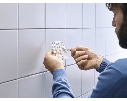 Personne retirant le film protecteur des bandes adhésives devant des carreaux blancs