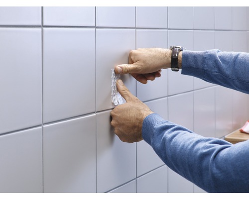 Du ruban adhésif double face est fixé sur un carreau mural.