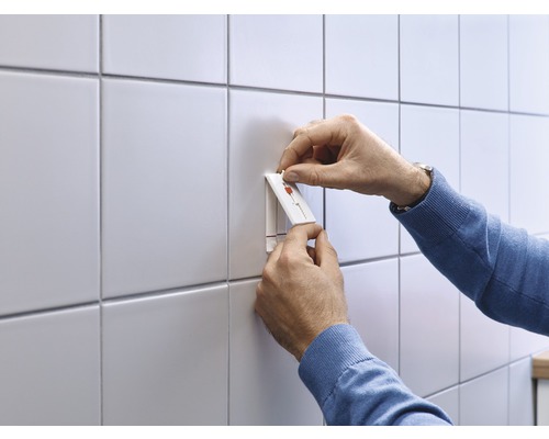 Personne fixant un crochet autocollant sur un mur carrelé