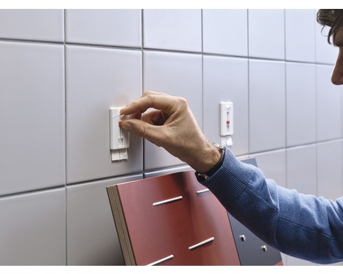 Une personne fixe un crochet adhésif sur un mur carrelé