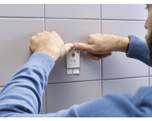 Un homme fixe un système de fixation sur un mur carrelé
