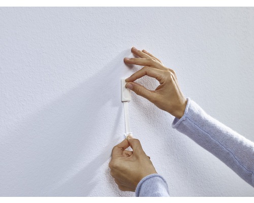 Eine Person befestigt einen Klebestreifen an einer Wand.