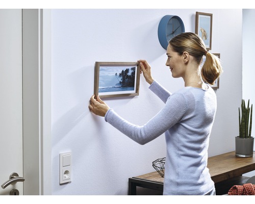 Frau hängt Bilderrahmen an Wand in einem Wohnraum