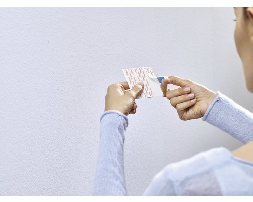 Eine Frau löst die Schutzfolie von einem doppelseitigen Klebestreifen.