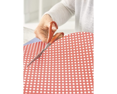 Person schneidet Papier mit Punktdesign mit einer Schere.