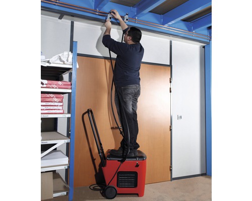 Un homme debout sur un déshumidificateur installe une conduite au plafond