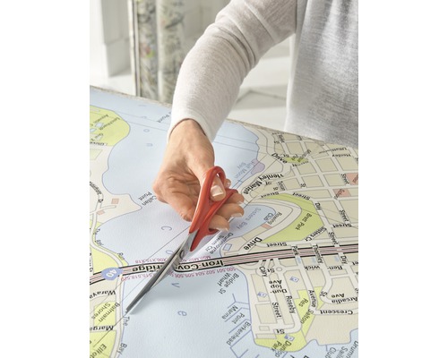 Eine Person schneidet eine Landkarte mit einer Schere.