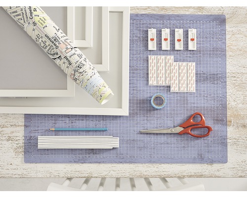 Szene mit Bilderrahmen, Stadtplanrolle, Schneidematte, Klebestreifen, Klebeband, Bleistift, Gliedermaßstab und Schere.