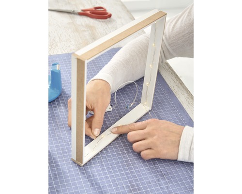 Person befestigt eine Lichterkette an einem dreieckigen Holzrahmen