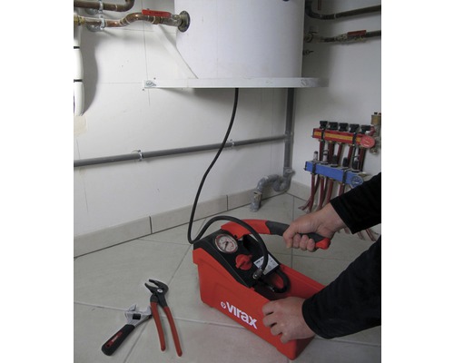 Une pompe d''épreuve avec manomètre est actionnée par une personne, tandis qu''une clé serre-tube et une clé à molette sont posées à côté.