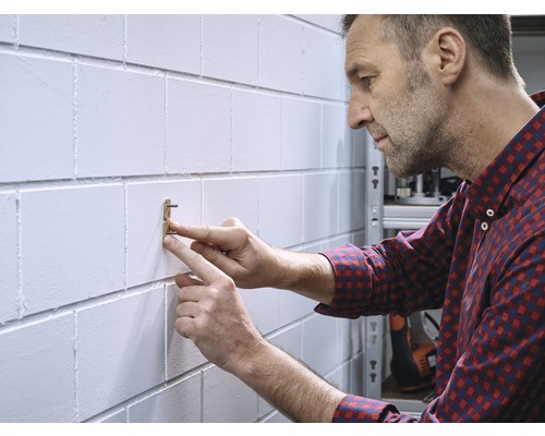Un homme fixe une étagère murale avec un clou sur un mur en parpaings de béton.