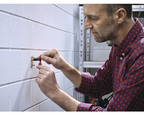 Un homme fixe une cheville à un mur.