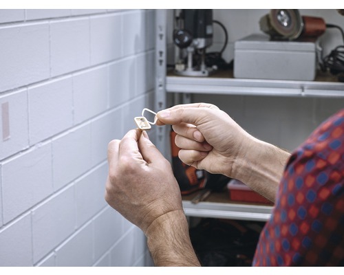 Une personne fixe une fermeture magnétique autocollante sur un mur.