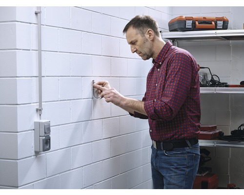 Un homme fixe un support sur un mur en maçonnerie dans un atelier.