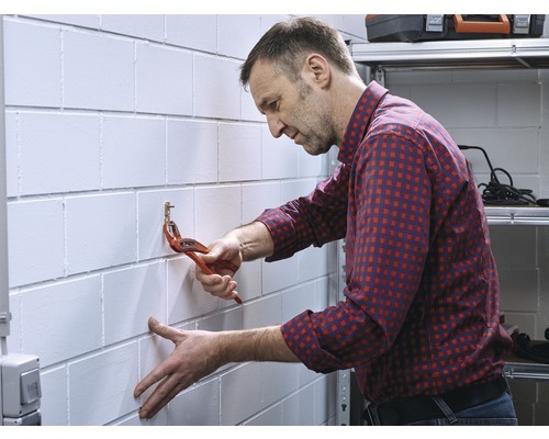 Un homme fixe un crochet au mur avec une pince multiprise.