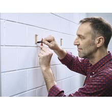 Un homme fixe une tringle à vêtements sur un mur de briques blanches.