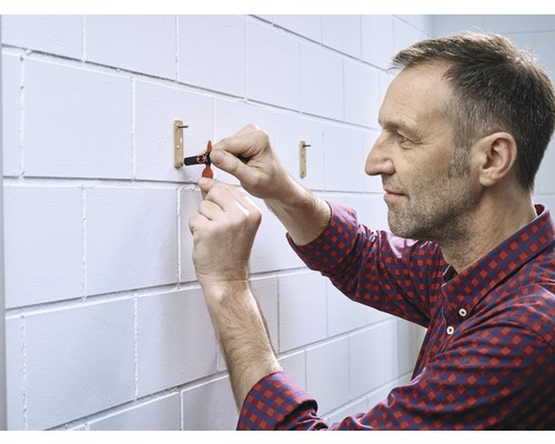 Un homme fixe une tringle à vêtements sur un mur de briques blanches.