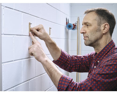 Un homme fixe un crochet en bois à un mur