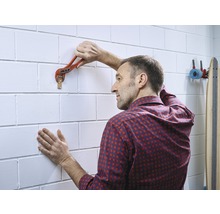Un homme fixe un crochet mural à un mur de briques à l''aide d''une clé serre-tube