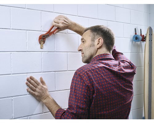 Un homme fixe un crochet mural à un mur de briques à l''aide d''une clé serre-tube