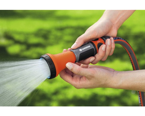 Une personne tient un tuyau d''arrosage avec une lance d''arrosage à la main, d''où jaillit de l''eau.