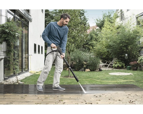 Un homme nettoie une terrasse en bois avec un nettoyeur haute pression
