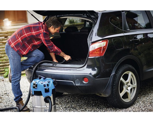 Ein Mann saugt den Kofferraum eines Autos mit einem Nass Trockensauger.