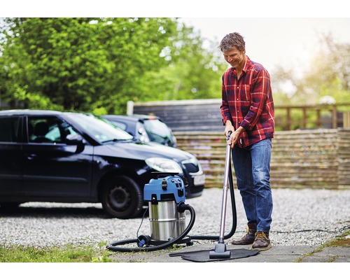 Mann saugt mit einem Nass Trockensauger eine Fußmatte vor einem Auto.