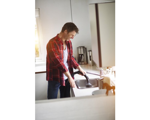 Ein Mann reinigt ein Spülbecken mit einem Staubsauger in einer hellen Küche.