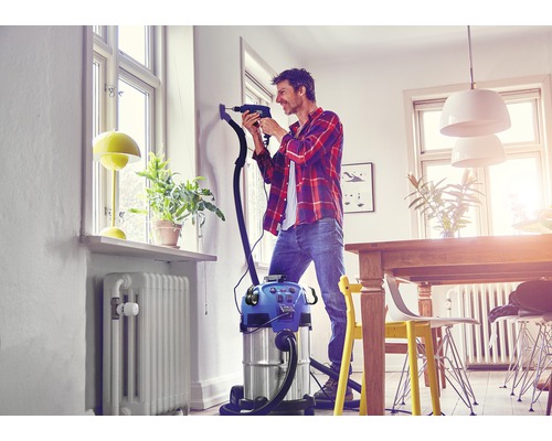 Mann bohrt mit Staubsauger in einer hellen Wohnung ein Loch in die Wand