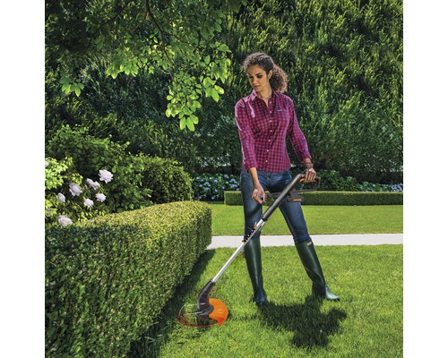 Femme coupant une haie avec un coupe-bordures dans le jardin.