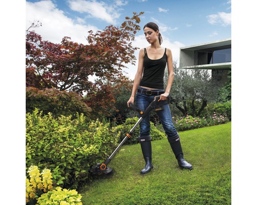 Frau arbeitet mit einem Rasentrimmer im Garten.