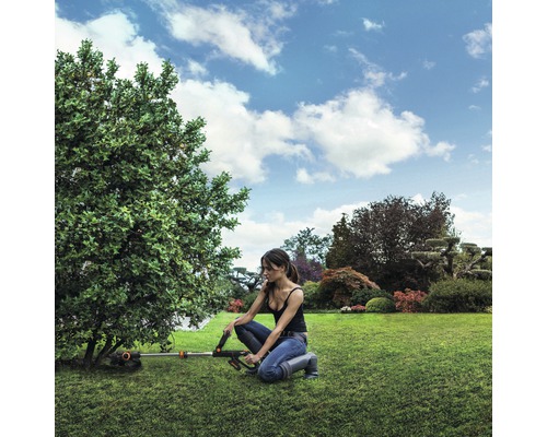 Frau arbeitet mit einem Akku-Rasentrimmer im Garten an einem Baum