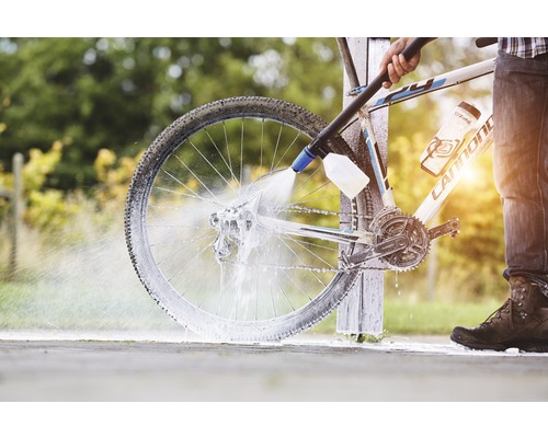 Eine Person reinigt ein Fahrrad mit einem Hochdruckreiniger.
