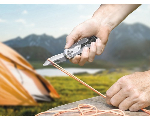 Person schneidet Seil mit einem Taschenmesser in der Natur.