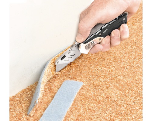 Eine Hand schneidet mit einem Universalmesser einen Teppich