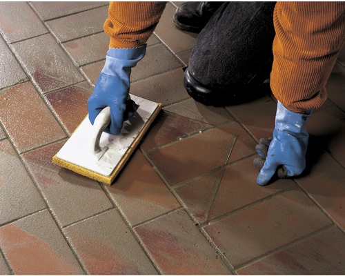 Eine Person verfugt Pflastersteine mit einem Fugbrett und Handschuhen.